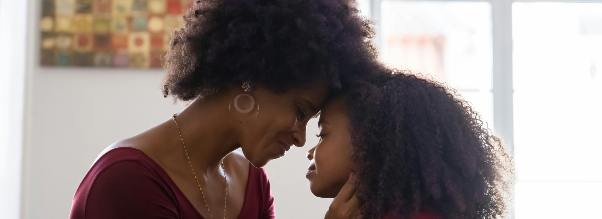 Mother and daughter with foreheads touching, sharing a tender moment indoors.