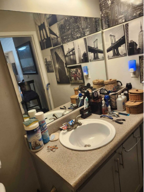 Cluttered bathroom counter with sink, wall collage, mirror, and items.