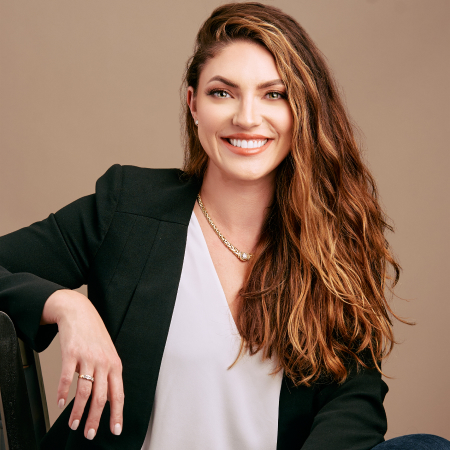 Professional woman with long wavy hair in a blazer, smiling at camera.