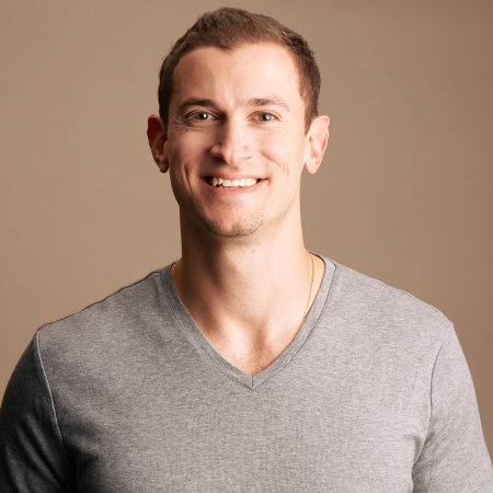 Smiling man with short brown hair in a gray V-neck shirt against a beige background