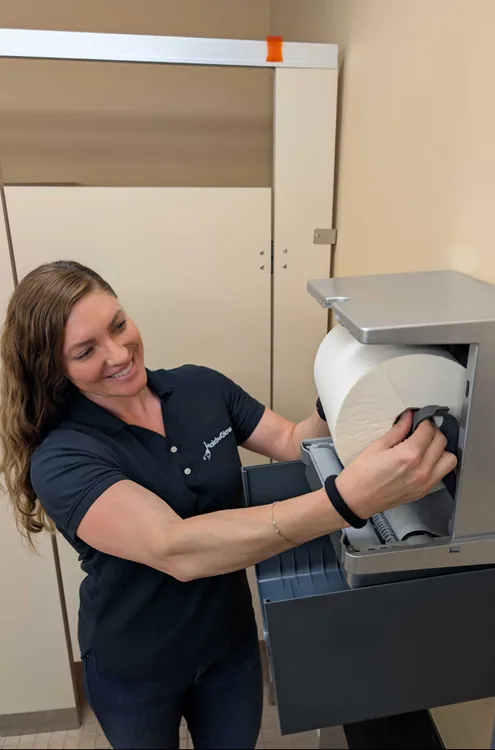 Smiling woman loading a roll of paper into a large clinical printer or copier.