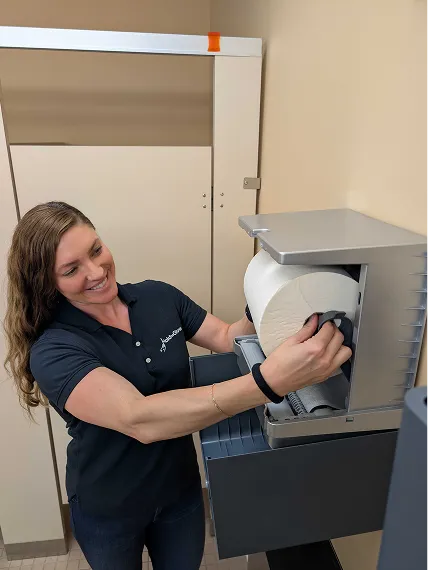 Woman operating a large industrial printer, loading a roll of paper.