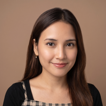 Portrait of a young woman with long brown hair, wearing a black top and checkered dress, against a beige background.
