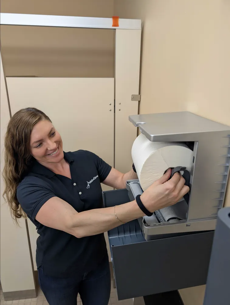 Woman loading a large roll of paper into a gray lab printer in a beige room.